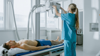 In the Hospital, Man Lying on a Bed, Female Technician adjusts X-Ray Machine. Modern Hospital with...