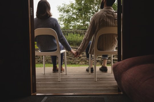 Rear view of couple holding hands while sitting on chair