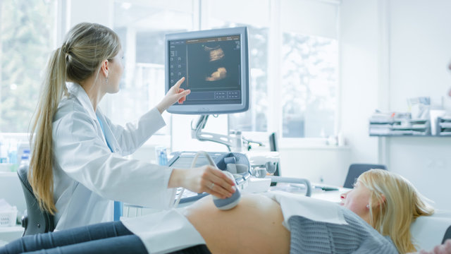 In the Hospital, Obstetrician Uses Transducer for Ultrasound/ Sonogram Screening / Scanning Belly of the Pregnant Woman and Points Finger at Screen. Screen Shows 3D Image of forming Baby.