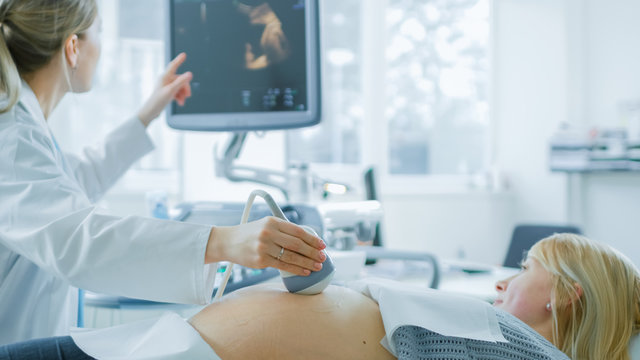 In the Hospital, Obstetrician Uses Transducer for Ultrasound/ Sonogram Screening / Scanning Belly of the Pregnant Woman and Points Finger at Screen. Screen Shows 3D Image of the Healthy Forming Baby.