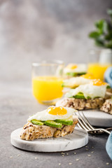 Healthy sandwich with fresh avocado and fried quail egg on small marble board on gray background. Breakfast or lunch food concept with copy space.