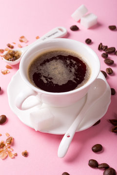 White cup of coffee with coffee beans, candy sugar and spices on pink background.