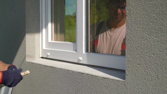Closeup worker in safety glasses sweeping surface for metal sill installation. Builder cleaning workplace for assembling PVC window construction outside building. Technology, exterior design concept