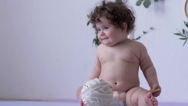 curly little girl eats cookie and waving plump hands on photo session in studio