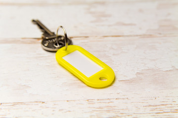 Yellow key tag on a light tree textured background.The concept of renting, selling. Template. Trend colors