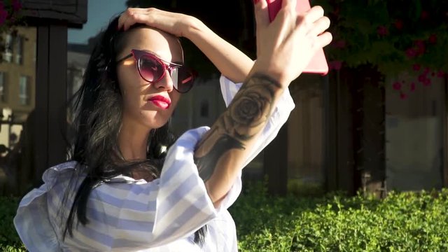 Stylish brunette in sunglasses with tattoo on hand make selfie at her phone