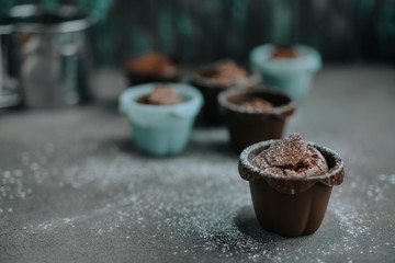 Appetizing chocolate brownie cupcakes sprinkled with powdered sugar in confectionery molds of brown and blue colors. Close up. Selective focus.