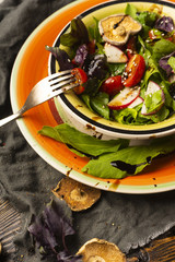 Salad serving from basil, sorrel, pieces of radish and cherry tomatoes, poured with a sauce in a dish on an old wooden table