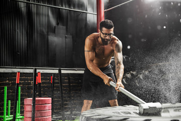 Man is hitting tire with a sledgehammer during his cross training workout