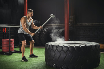 Man is hitting tire with a sledgehammer during his cross training workout
