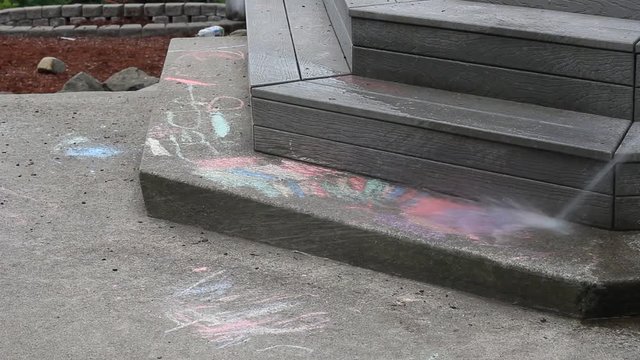 A hose is used to remove sidewalk chalk that the kids drew allover the ground.