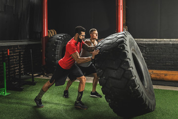 Two strong men doing  a tire flip exercise