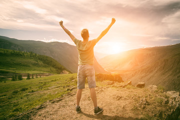 Man with a backpack standing on top of a mountain. Raising your hands and enjoying the sunrise in the valley