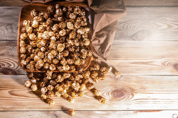 Caramel popcorn in a wooden bowl on a wooden background. Low key lighting. Selective focus. Top view