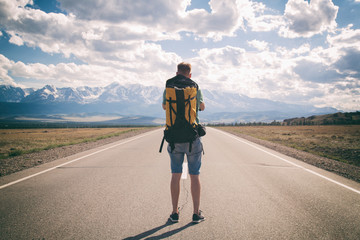 Man is standing on an asphalt road with a backpack on his back. Mountain View