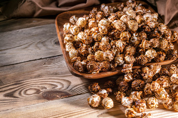 Caramel popcorn in a wooden bowl on a wooden background. Low key lighting. Selective focus. Close-up