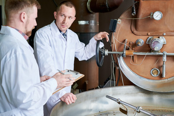 Waist up portrait of two modern young men wearing lab coats discussing coffee processing while working in roastery, copy space