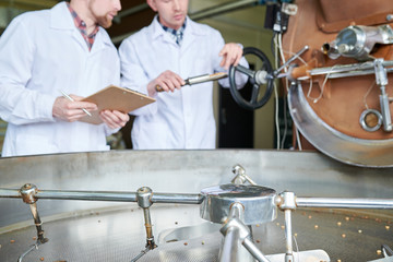 Mid-section portrait of two unrecognizable modern young men wearing lab coats discussing coffee processing while working in roastery, copy space