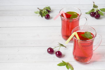 Cherry juice with mint leaves and fresh cherries on a white wooden table. Copy space