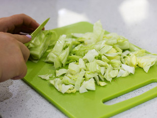 Hands cut a lettuce salad with a knife on a green board