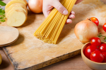 Chef put raw spaghetti on chopping board with tomatoes and onion, prepare ingredient before cook a pasta at restaurant. Cook Italian food and culinary concept.