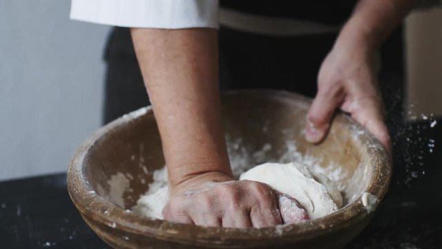 Slow motion shot of baker hands kneading dough in flour in wooden bowl