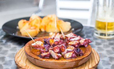 Wooden plate of galician style cooked octopus with potatoes, paprika and olive oil. Pulpo a la gallega