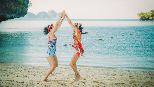 Two happy young woman jumping and laughing on the beach