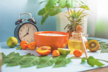 Useful morning breakfast, muesli, fruit Peaches Lime Pineapple Honey Cup of coffee and an alarm clock on a blue background Close up