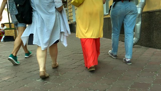 Three women in stylish clothes are walking along the sidewalk of the city. Fragment of feet. Close-up.