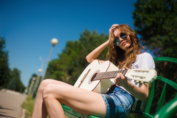 Beautiful young hipster girl playing guitar outdoors in the Park