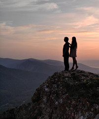 A man and a woman stand on top of the mountain at sunset.