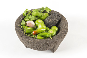 Mexican mortar and pestle used for preparing hot sauce Green peppers and tomatoes used to make green Mexican sauce