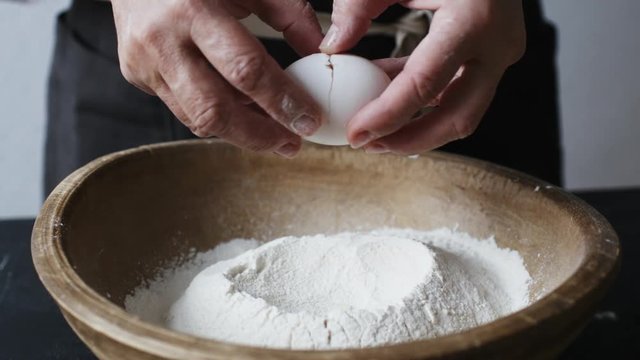 Slow motion shot of egg falls on wooden bowl with flour.