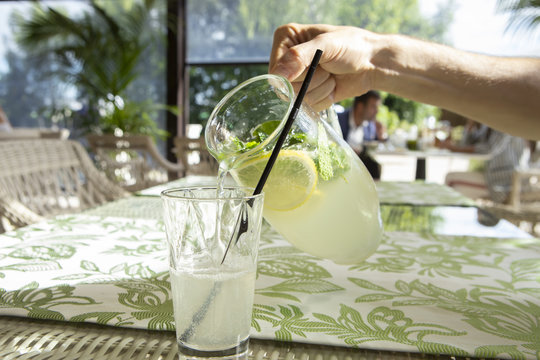 Lemonade with lemon, mint and ice. Young man pouring lemonade into glass.
