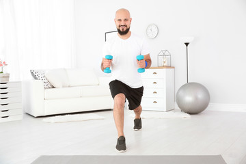 Overweight man doing exercise with dumbbells at home