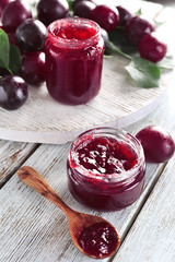 Glass jar with delicious plum jam on wooden background