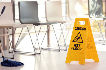 Safety sign with phrase Caution wet floor and mop, indoors. Cleaning service