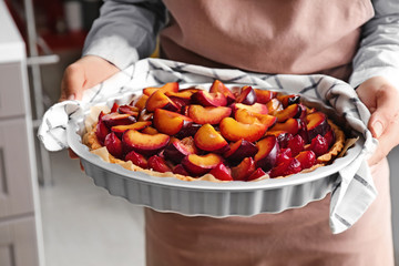 Woman holding delicious pie with plums, closeup