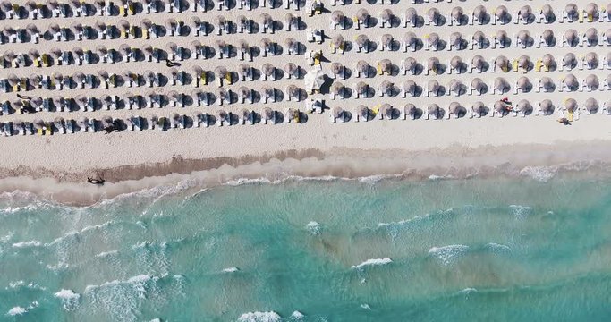 Aerial - Umbrellas on the beach. Top down view of waves hitting sandy shore