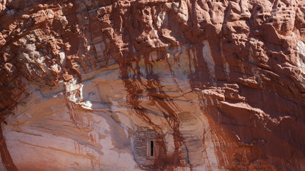 A small window in a cliff face of white sandstone streaked with red from the ground up above