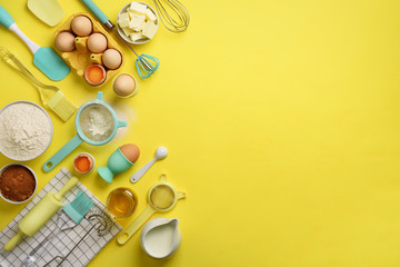 Butter, sugar, flour, eggs, oil, spoon, rolling pin, brush, whisk, towel over yellow background. Bakery food frame, cooking concept. Ingredients on kitchen table. Top view, copy space. Flat lay