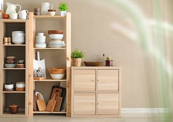 Storage stand with ceramic and wooden kitchenware on light wall background
