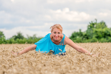 Naklejka na ściany i meble Portrait of a smiling happy woman in a ripe wheat field. Wide spread arms.