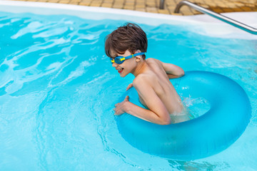 side view of happy boy in swimming glasses with inflatable ring swimming in swimming pool on summer day