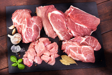 Sliced raw pork meat with spices, served on the slate plate, on wooden background. Top view.