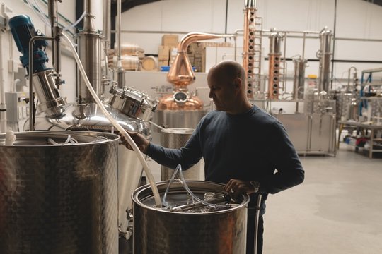 Worker filling alcoholic drink in drum at factory&dagger;