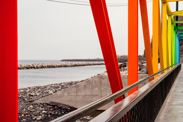 A contemporary brightly coloured metal rainbow truss bridge over a sea inlet in Tenerife.