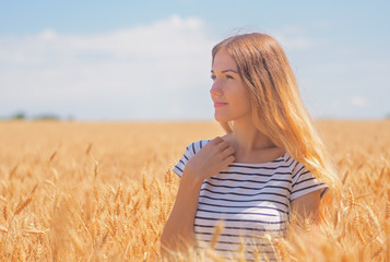 Fototapeta na wymiar Young woman at the wheat field under the blue sky at the sunny day