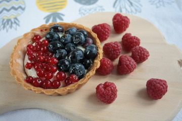 A tartlet with seasonal fruits surrounded by raspberries
